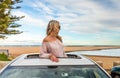 Road trip summer beach vibes. Carefree woman in sunroof car by beach