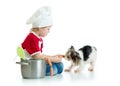 Role-playing game. Kid boy plays chef with dog. Child weared cook feeds hungry puppy.