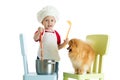 Role-playing game. Kid boy plays chef with dog. Child weared cook feeds hungry puppy.