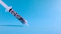 A roll of 100 dollars money inserted into a white medical hypodermic needle on a blue background. The concept of health care costs