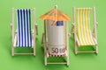 A roll of euro notes lies in a lounge chair, under an umbrella, as if resting, beside it stand two empty lounge chairs