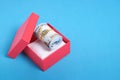 Roll of hundred dollar bills in red gift box on blue background Royalty Free Stock Photo