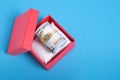 Roll of hundred dollar bills in red gift box on blue background Royalty Free Stock Photo