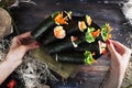 Roll sushi black different tastes, hands, tray, dish crab, carrots, lettuce, tofu, salmon, still life, home, stylish, wooden Royalty Free Stock Photo