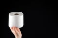 A roll of white soft toilet paper in a man's hand on a black background with space for text Royalty Free Stock Photo