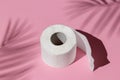 Roll of a white toilet paper isolated on a pink background under a palm tree shadow close-up. hard shadows from the sun at noon Royalty Free Stock Photo
