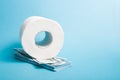 A roll of white toilet paper and a stack of 100 dollar bills blue background Royalty Free Stock Photo