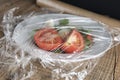 Roll of wrapping plastic stretch film over plate of vegetabes. Close-up isolated on wooden background. No plastic concept. Zero we