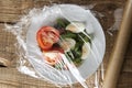 Roll of wrapping plastic stretch film over plate of vegetabes. Close-up isolated on wooden background. No plastic concept. Zero we