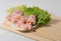 Rolled bacon slices are placed on a lettuce leaf on a plate. Bamboo cutting Board and texture table as background Royalty Free Stock Photo