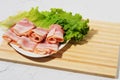 Rolled bacon slices are placed on a lettuce leaf on a plate. Bamboo cutting Board and texture table as background Royalty Free Stock Photo