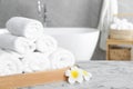 Rolled bath towels and beautiful flowers on white marble table in bathroom, space for text Royalty Free Stock Photo