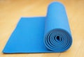 A rolled blue exercise mat for Yoga or Pilates on wooden floor
