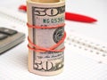 Rolled bundle of dollars stands near the calculator. Close-up Royalty Free Stock Photo