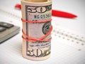 Rolled bundle of dollars stands near the calculator. Close-up