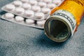 Rolled Money Bills in orange pill bottle and pills on table. Money for healthcar Royalty Free Stock Photo