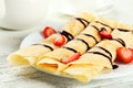 Rolled pancakes with strawberry on plate on white wooden background.