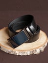 Rolled-up black fashionable men`s leather belt with automatic buckle on wood slice on brown background. Male accessory. Front vie Royalty Free Stock Photo
