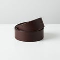 A rolled-up dark brown leather belt with a smooth texture is positioned on a white Royalty Free Stock Photo