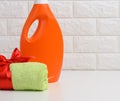 A rolled up terry green towel tied with a red silk ribbon and an orange plastic bottle of liquid laundry detergent on a white Royalty Free Stock Photo