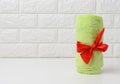 Rolled up terry green towel tied with red silk ribbon on white shelf in bathroom