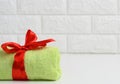 Rolled up terry green towel tied with red silk ribbon on white shelf in bathroom, copy space