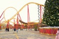 The roller coaster ride with thrill-seekers on the background of the New Year tree.