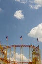 Roller coaster with waving flag photographed upwards against the bright and blue sky with sun and small white clouds Royalty Free Stock Photo