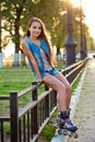 Roller girl wearing jeans sitting on iron fence