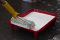 Roller in white paint. A painter applies paint to a roller with a handle