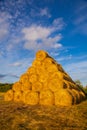 Rollers made of dry pressed yellow straw, stacked in a pyramid in a field, against a blue sky