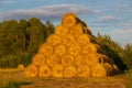 Rollers made of dry pressed yellow straw, stacked in a pyramid in a field, against a blue sky