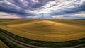 Rolling golden wheat fields stretch towards the horizon under a dramatic sky with sunbeams breaking through dark clouds, showing Royalty Free Stock Photo