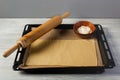 Rolling pin and baking sheet with dough and filling sits in a black oven tray