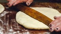 Rolling pin in hands, rolling dough on the wooden table, close-up.