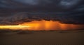 Rolling sand dunes stretch across the foreground under a dramatic, dark cloud Royalty Free Stock Photo