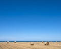 Rolls of straw on field under blue sky with ocean in the background in french normandy Royalty Free Stock Photo