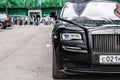 Rolls-Royce Ghost first generation stands on parking slot. Front half view. Modern city at background