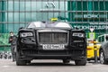 Rolls-Royce Ghost first generation stands on parking slot. Front view of black premium sedan. Modern city at background