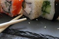 Rolls with shrimp, crab stick, cheese, cucumber, vegetables and sushi sticks on a black board. Close-up. Royalty Free Stock Photo