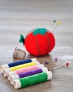 Rolls of thread with an out of focus pin cushion shaped as a red tomato and a thimble