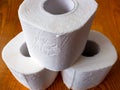 3 rolls of toilet paper stands in the shape of a pyramid on a brown wooden table Royalty Free Stock Photo