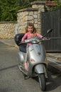 ROMA, ITALY - AUGUST 2018: Little beautiful girl driving a scooter Vespa in the antique Italian streets Royalty Free Stock Photo