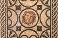 Close-up on roman mosaic portraiting a chubby medusa face surrounded by ancient decorative pattern