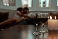 Romance never gets old. Wine glasses and candles on table with couple relaxing in the background on couch Royalty Free Stock Photo