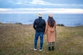 Romance scene of young heterosexual couple view from back holding hands watching the horizon on the sea - Two unrecognizable