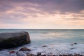 Romantic atmosphere in peaceful morning at sea. Big boulders sticking out from smooth wavy sea. Pink horizon Royalty Free Stock Photo