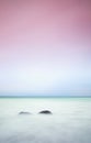 Romantic atmosphere in peaceful morning at sea. Big boulders sticking out from smooth wavy sea. Pink horizon Royalty Free Stock Photo