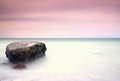 Romantic atmosphere in peaceful morning at sea. Big boulders sticking out from smooth wavy sea. Pink horizon Royalty Free Stock Photo