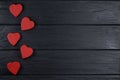 The romantic background with five red wooden hearts on a black wooden background.